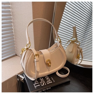 Detail of a creamy beige half-moon handbag with gold circular clasp on books