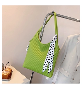 Detail of green pleated baguette bag with a polka dot scarf on a metal stand