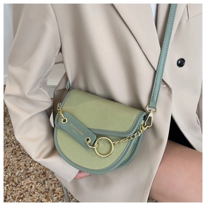 Detail of avocado green saddle bag with crocodile pattern and golden metal chain