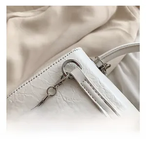 Close-up of silver metal hook and stitching on white textured leather square bag