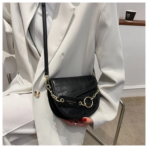 Detail of black crocodile texture saddle bag with gold metal chain and ring on model