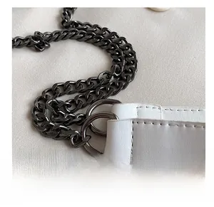 Détail de la chaîne en métal foncé et de la bandoulière en cuir blanc avec surpiqûres