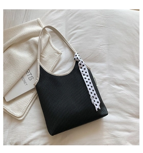 Detail of black pleated underarm bag with cream strap and polka dot scarf accessory
