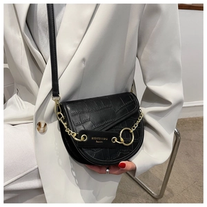 Detail of black crocodile embossed saddle bag with gold metal chain and brand logo