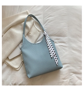 Close-up of light blue pleated shoulder bag with polka dot scarf and fashion label