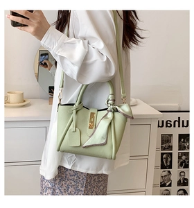Dettaglio borsa a secchiello verde chiaro in pelle martellata con chiusura oro e foulard