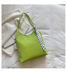 Close-up of green pleated shoulder bag featuring a polka dot scarf and knit texture