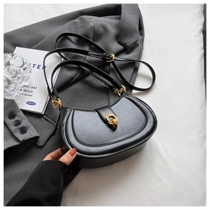 Detail of black matte leather saddle bag featuring a gold double-ring buckle and strap