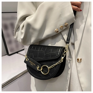 Detail of black crocodile texture saddle bag with golden chain and magnetic flap closure