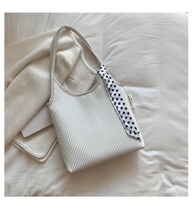 Detail of white pleated tote bag featuring fashion label and decorative polka dot scarf