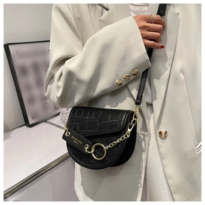 Detail of black crocodile texture saddle bag with gold ring and chain on white blazer
