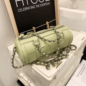 Mint green woven cylinder crossbody bag with chunky chain strap on a white stand