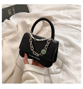 Detail of black crossbody bag with pleated flap, pearl chain, and floral typography