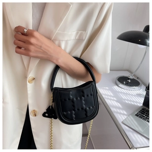 Detail of black crossbody bag with quilted texture, gold chain and stylish ornament