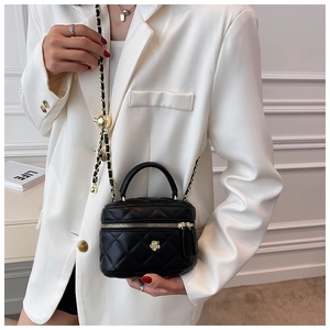 Detail of mini black quilted bag featuring gold camellia hardware and chain strap