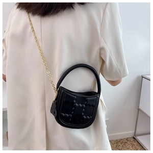 Detail view of black textured mini crossbody bag with gold chain and bear charm on model