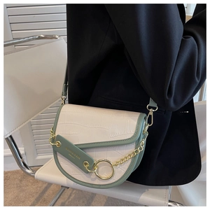 Detail of a cream faux-crocodile saddle bag with green trim and gold chain on a chair