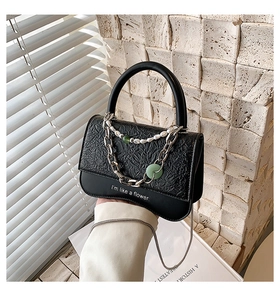 Detail of black textured handbag with pearl chain decoration and flower typography
