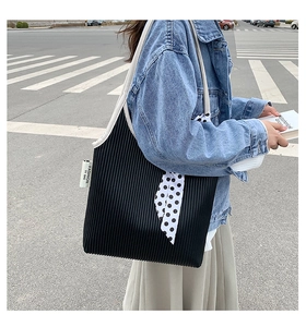 Detail of black pleated shoulder bag with white strap and polka dot silk scarf decoration