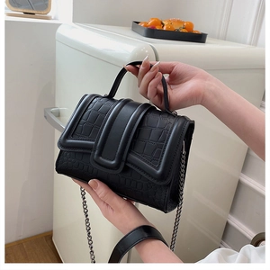 Détail du sac à main noir à motif crocodile avec chaîne en métal et rabat en forme de U