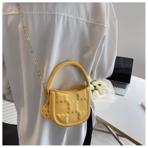 Detail of yellow embossed lattice mini bag with gold chain and bear charm in office setting