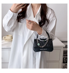 Detail of black crossbody bag featuring embossed texture and silver chain with pearl accents