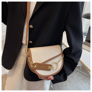 Detail of white crocodile pattern saddle bag with brown trim and gold chain strap