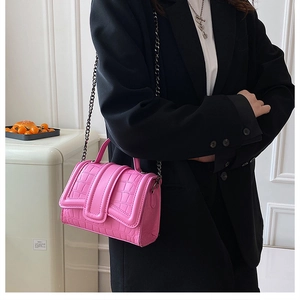 Détail d'un sac à main carré rose façon croco avec chaîne en métal noir sur mannequin femme