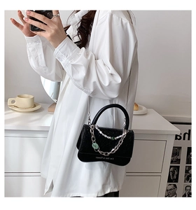 Detail of black mini crossbody bag featuring pearl charms and green ring accents
