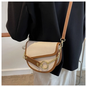 Detail of a white crocodile-embossed saddle bag with brown trim and gold chain strap
