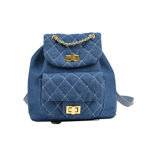 Sac à dos en denim bleu avec surpiqûres en losange blanc et détails dorés sur fond blanc
