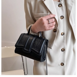 Détail du sac noir motif crocodile avec chaîne argentée porté sur un gilet beige