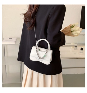 Detail showing the white textured crossbody bag with pearl chain and flower text print