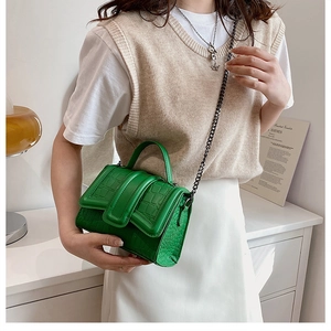 Détail du sac à main vert à texture crocodile avec chaîne porté par un mannequin