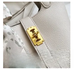 Dettaglio borsa a secchiello in pelle crema con chiusura dorata e foulard in seta
