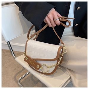 Detailed close-up of a white croc-embossed saddle bag with brown trim and gold metal rings
