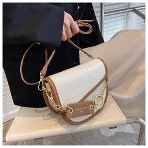 Detail of white crocodile pattern saddle bag with brown trim and gold chain links