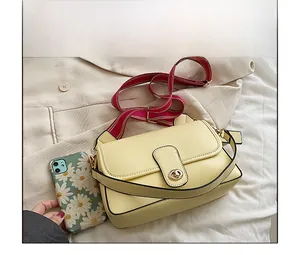 Détail du sac bandoulière jaune avec fermoir rotatif doré et bandoulière en tissu rayé