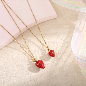 Dettaglio macro di due collane con ciondolo a fragola in smalto rosso e oro