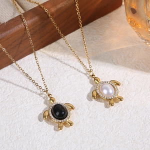 Détail de pendentifs tortue avec chaînes dorées, pierre noire et perles blanches