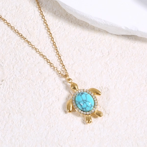 Gros plan du pendentif tortue dorée avec une pierre turquoise et cristaux blancs