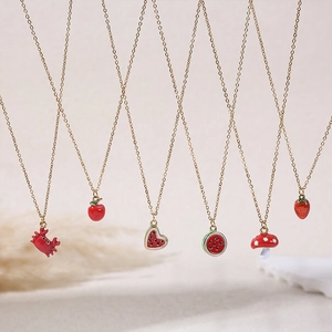 Detail of red enamel fruit and animal pendants on delicate golden stainless steel chains