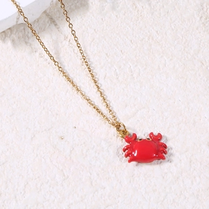 Detail of a gold chain necklace featuring a vibrant red enamel crab pendant on stone