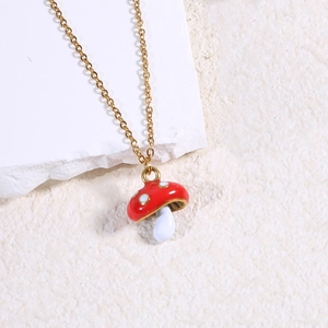 Macro shot of gold necklace with a red and white mushroom enamel pendant on stone