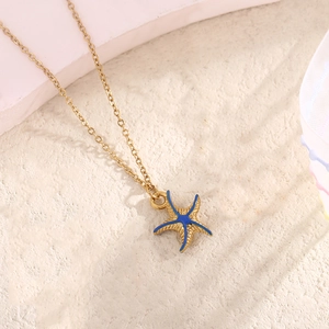 Close-up of golden starfish pendant with bright blue enamel on a soft textured background