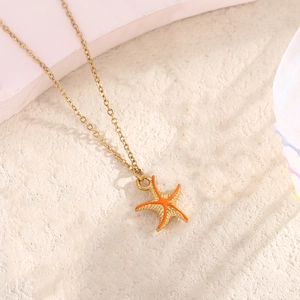 Macro detail of gold starfish pendant with orange enamel on minimalist link chain
