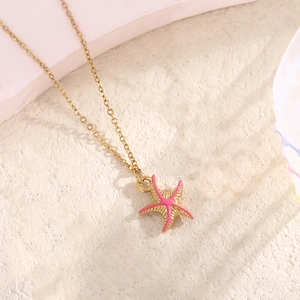 Detailed view of gold starfish pendant with pink enamel finish on sleek stone surface