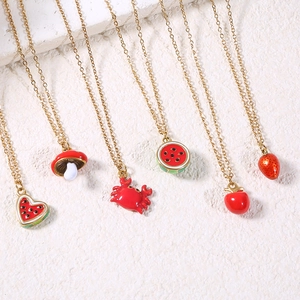 Golden necklace set with red enamel watermelon, crab, and mushroom charms on white surface
