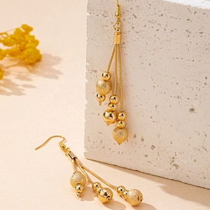 Elegant gold tassel earrings with polished and frosted beads on a textured stone base