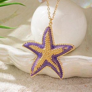 Bohemian gold starfish pendant necklace with purple enamel on a sandy beach background